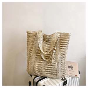 Detailed close-up of beige woven straw tote bag with white bead tassels on a white suitcase