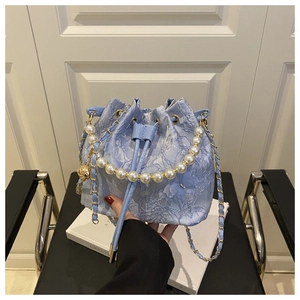 Close-up of light blue lace bucket bag with pearl handle and golden chain strap detail