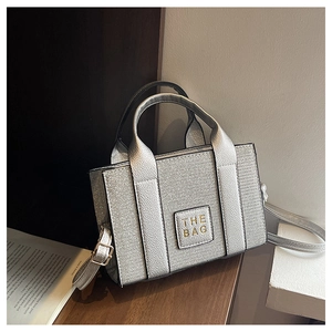 Close-up of small silver tote bag with lychee texture and metallic THE BAG label