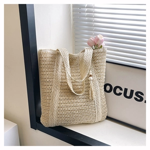 Detail of hand-woven beige straw tote bag featuring decorative wooden bead tassel and soft lighting
