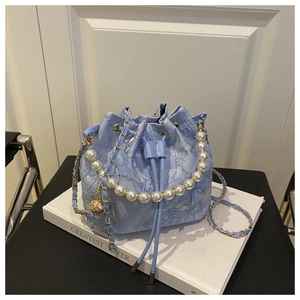 Détail du sac seau en dentelle bleu clair avec anse en perles et texture de chaîne dorée