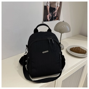 Detail of a black nylon backpack with metal logo and adjustable wide woven straps