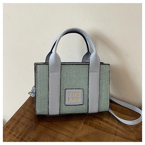 Detail of light green woven mini tote bag featuring light blue handles and THE BAG logo