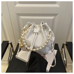 Detail of white lace bucket bag with pearl handle and golden chain strap on a chair