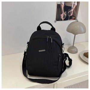 Detail view of black nylon backpack with metal logo plaque and adjustable straps