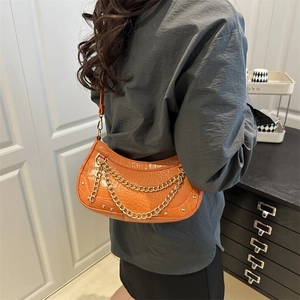 Orange croc-embossed crescent bag with gold chain strap worn by a model