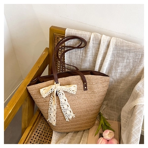 Détail du sac seau en paille tressée avec bandoulières en cuir marron et nœud en dentelle