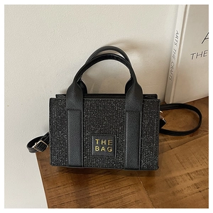 Macro detail of black sequin tote bag with The Bag leather patch and metallic finish