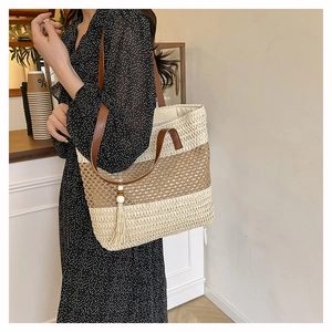 Detail of a beige woven tote bag with brown leather handles and decorative tassel accent