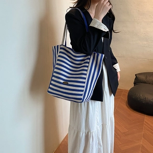 Minimalist blue and white striped canvas tote bag shown on model in a modern interior