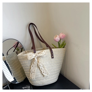Détail d'un sac cabas en paille avec nœud en dentelle beige et anses marron foncé