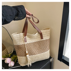 Detail of color-block straw tote bag featuring leather handles and a tassel bead charm