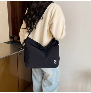 Détail d'un grand sac en nylon noir avec bandoulière tressée porté par un modèle