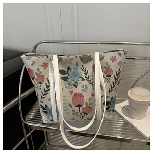 Détail du sac cabas vintage en tapisserie florale avec des anses en cuir blanc sur socle