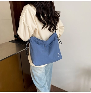 Blue nylon tote bag detail with black and white striped rope shoulder strap worn by model