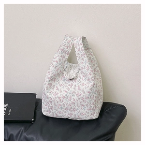 Detail der floralen Stoff-Beuteltasche mit weichen Griffen auf schwarzem Hintergrund