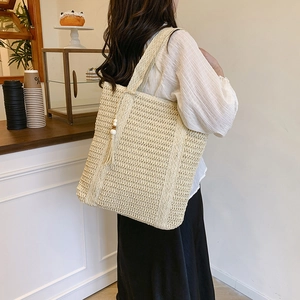 Beige woven tote bag with fringe wood bead tassel displayed in a cafe setting