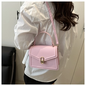 Close-up of pink crossbody bag with gold lock buckle and top handle on a model
