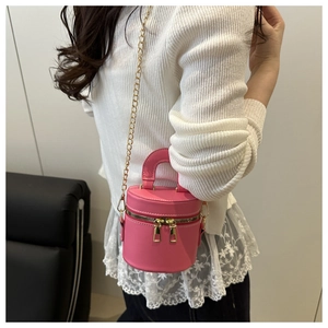 Sac seau cylindre rose avec chaîne dorée porté par un mannequin pour un look d'été chic
