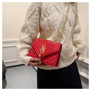 Red quilted chain crossbody bag with gold S-buckle and tassel on a white knit sweater