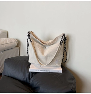 Gros plan du sac fourre-tout beige montrant la texture, le bouton et la bandoulière tressée