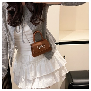 Detail of a brown mini handbag featuring a decorative silver metal bow clasp and chain strap