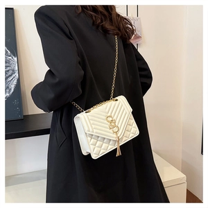 Detail of white quilted handbag with gold S-logo and fringe tassel on black coat