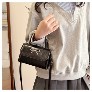Détail du mini sac noir avec nœud argenté et bandoulière en cuir poli brillant
