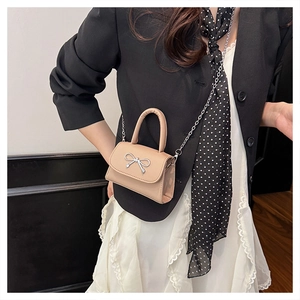 Detail of beige leather mini crossbody bag with silver metal bow and fine chain strap