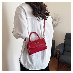 Modèle portant un sac bandoulière en cuir verni rouge avec un nœud argenté