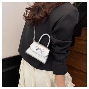 Silver mini crossbody bag with a metal chain and a decorative bow on black blazer