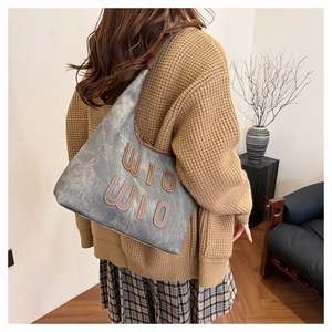 Détail du sac bandoulière gris en forme de croissant avec texture vintage et lettres en cuir