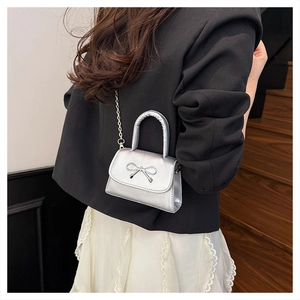 Detail of silver metallic handbag featuring bow clasp and chain strap on a model