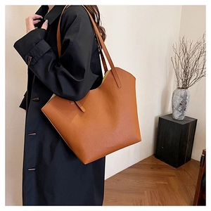 Dettaglio di una grande borsa tote marrone caramello con bordo curvo e texture fine
