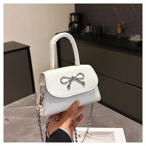 Detail of white square handbag with silver bow hardware and metallic chain strap