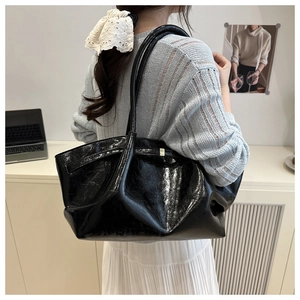 Detailed view of a black high-gloss patent leather tote bag on a model shoulder