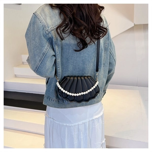 Close-up of black shell-shaped bag with pleated leather texture and elegant pearl trim