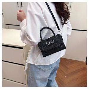 Detail of black glitter mini bag with silver bow buckle on model in bright interior