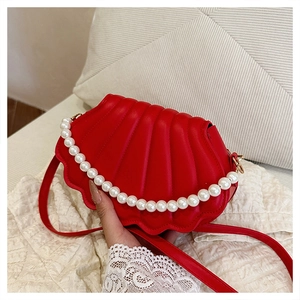 Detail of red shell-shaped bag featuring pleated PU texture and elegant pearl handle