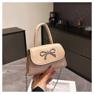 Detail of minimalist beige handbag featuring a decorative silver metallic bow and fine chain