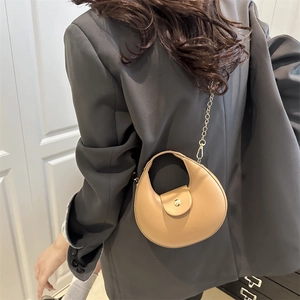 Minimalist beige crescent bag with gold chain strap worn over a grey blazer
