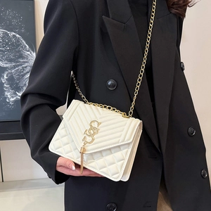 White quilted flap square bag with gold chain strap and tassel, shown on black blazer