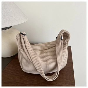 Detailopname van beige corduroy schoudertas met geribbelde textuur op een houten tafel