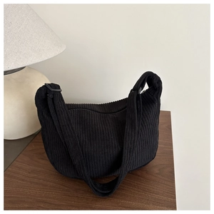 Detail van zwarte corduroy hobo-tas met verstelbare riem op een rustieke houten tafel