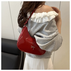 Detail of red patent leather crescent bag with silver bow on model’s shoulder