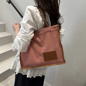 Pink corduroy tote bag with brown trim and leather patch shown on model in a staircase