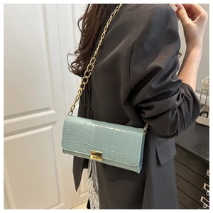 Detailed view of light blue crocodile pattern baguette bag with gold chain strap worn by model