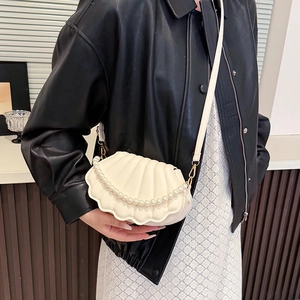 Chic cream seashell crossbody bag with pearl chain detail worn by model in leather jacket