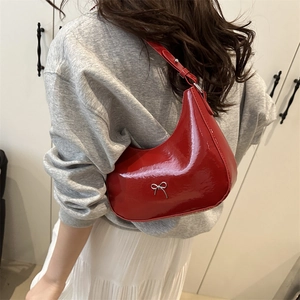 Red patent leather crescent bag with silver bow detail worn by a model