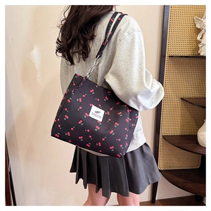 Close-up of black canvas tote bag featuring red cherry prints and stylish chain shoulder strap